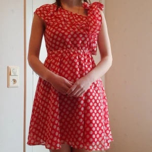 Polka Dot Klänning - Röd above-knee tyllklänning med vita prickar. Man kan knyta ena axelbandet eller lämna den off-shoulder. Märkt storlek M men sitter mer som en S. Har resår i midjan, stretchar dock inte så långt. Bra skick, kan hämtas i Stockholm :)