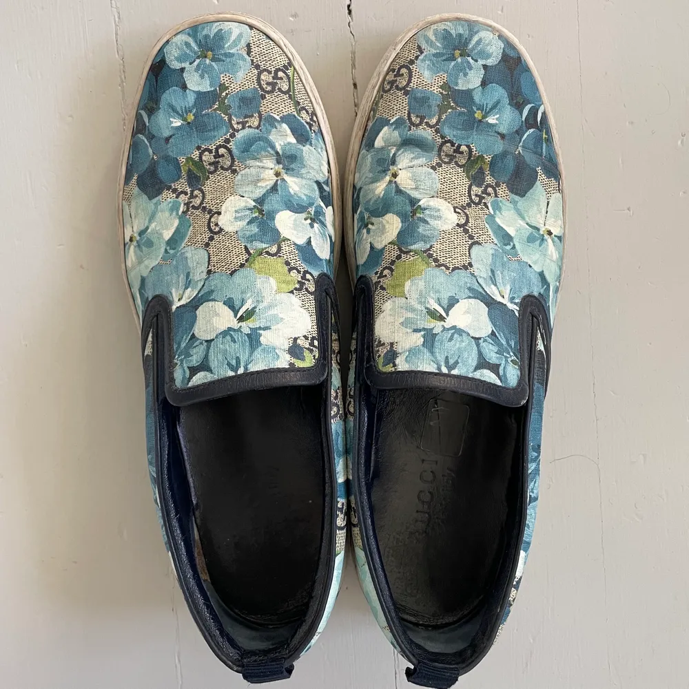 Säljer mina Gucciskor. Storlek 42 (US 8 1/2) Sneakers i slipp-on modell med monogram med blått blomster på. Utsidan är i canvas och insidan är i blått läder. Matchande kartong medföljer med dustbags.   Skorna är köpta 2017 på Gucci Woodbury Outlet utanför. Skor.