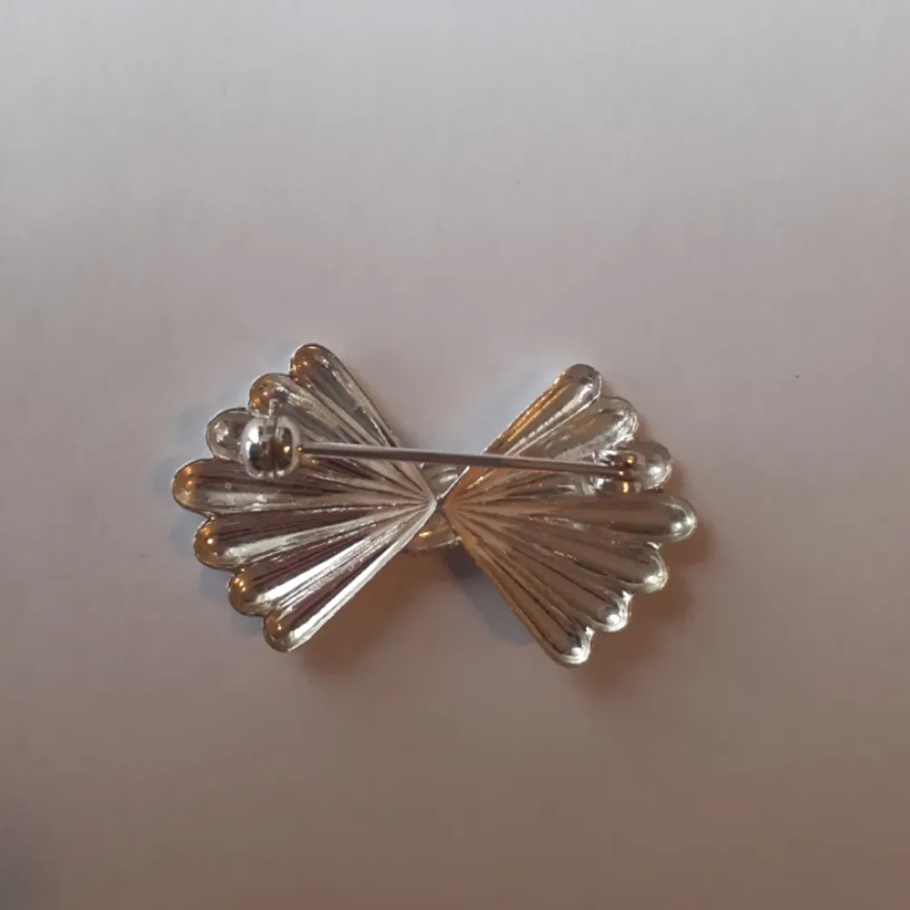 Brosch i äkta silver. Formad som en rosett och med knäppe baktill. Det finns 3 exemplar kvar och säljer dem för 100 kr/st Ask: 10kr (valfritt) Frakt: 15 kr. Asusteet.