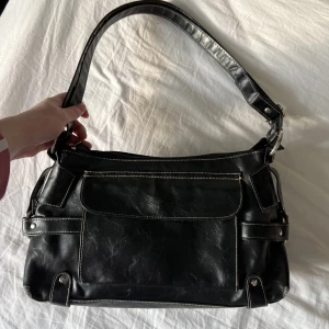 Läder Baguette väska  - Baguette väska i svart äkta läder köpt 2hand. Vita sömmar och justerbart band. Små slitningar vid kanterna på botten, men inget som stör. 