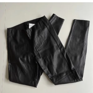 Skinnbyxor strl 34 - Oanvända skinnbyxor(fejk) med resår i midjan. Inga fickor, dragkedjor vid ankeln,  sömmar på fram och baksida. Storlek 34 från H&M. Superfina men för små för mig. Midja:66cm Innerben:73cm
