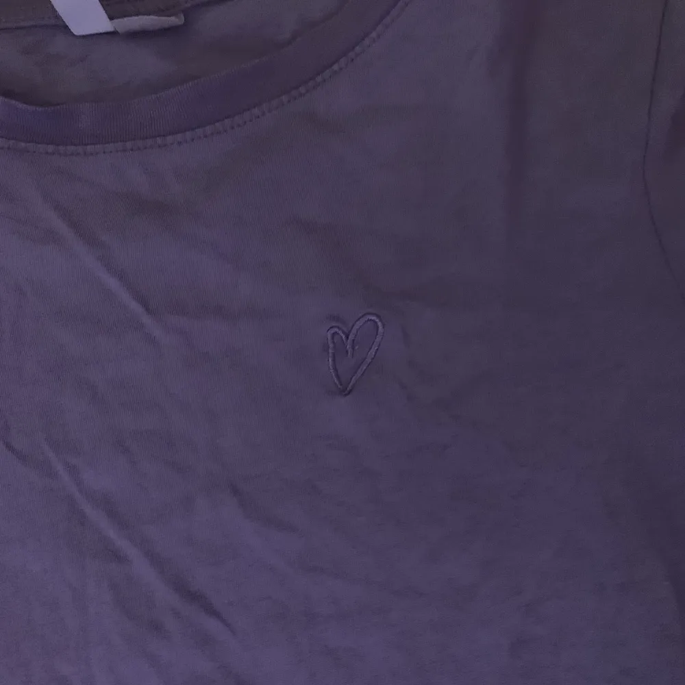 En lila T-shirt som har ett litet hjärta på sig uppe i hörnet.. T-shirts.