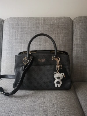 Guess hand samt axelväska.  - Hej! Säljer min Guess väska med avtagbar axelband. Väskan är knappt använd och är som ny. Dock är "Guess" loggan på framsidan i en rostfärg. Ingår även en mindre necessär inuti.  Väskan har 3 stora fack och 1 av dem går att stänga!