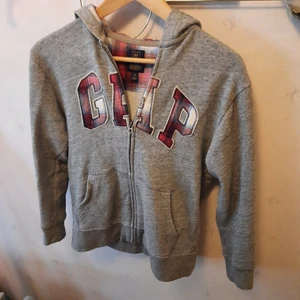 GAP Hoodie - GAP zipper hoodie med flannelmönster på loggan och i luvan. Köpt i London, Barnstorlek XL eller UK 12 och passar mig som är 165cm och brukar ha storlek S. Kan hämtas i Stockholm, annars står köpare för frakt :)
