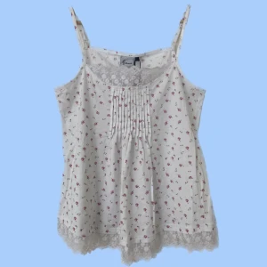 Blommigt linne - Blommigt linne med spetskant. Mycket stretch och justerbara axelband. Helt oanvänd, originallapp sitter på. Mycket bra skick. Storleken är L men kan även passa medium 