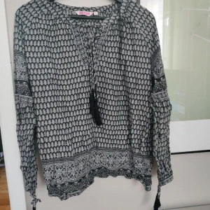 Tröja med mönster och fransar  - Fin tröja från Indiska. Med fransar och mönster i svart och grå. Knytning över bröstet. Storlek L men passar även M skulle jag säga.