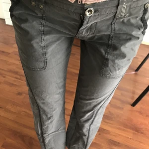 Cargobyxor - Lågmidjade utsvängda byxor. Små ränder på 💕Bra skick förutom att några rhinestones vid bälteshakarna har lossnat. Storlek 36, uppskattade till storlek 28. 🍀Mått runt midjan 82 cm. Innerbenslängd 72 cm. 🌟 Jag har W29 och är 177 cm lång, för korta för mig💛