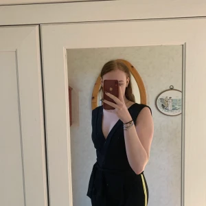 Jumpsuit - En svart jumpsuit i kostymmaterial med gul/vita detaljer på sidorna. V-ringad både fram och bak samt tajtare passform vid benen. (Aldrig använd) 💞