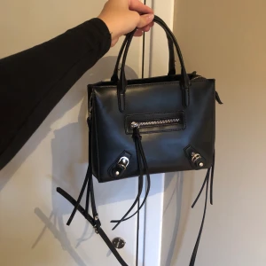 Svart väska  - En svart väska från Nelly som är jättefin. Har använt den men fortfarande i bra skick. Man kan justera axelbandet och även hur stor man vill ha den, och även bra fickor i. 