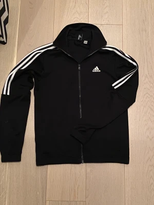 Adidas träningsjacka - Säljer min adidas jacka pga att storleken inte passar mig. Den är i superfint skick och har inte använts mycket alls. Det är syntet-/sportmaterial utan skador eller fläckar överhuvudtaget.
