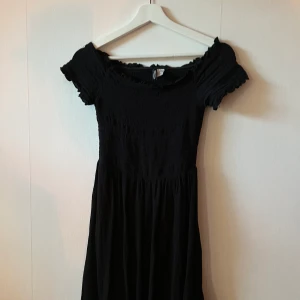 Svart klänning  - Svart knälång jättefin klänning med smock och off shoulder. Nyskick!