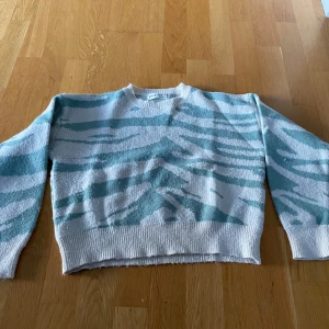 Vit och mintgrön stickad tröja Shein - Säljer en stickad tröja från Shein i vit och mintgrön zebra-mönster. Tröjan har rund halsringning, långa ärmar och ribbade muddar. Perfekt för dig som gillar unika mönster och mjuka material.