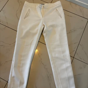 Vita kostymbyxor från H&M, strl 32 - Snygga vita kostymbyxor från H&M i storlek 32. Byxorna har raka ben, pressveck och diskreta fickor fram och bak. Lite nopprig på vissa delar av plagget, går enkelt bort med noppmaskin!