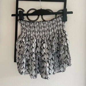 Svartvit volangkjol från Steele - Supersöt kort kjol från Steele i svartvitt mönster med bred smock i midjan och flera lager volanger. Kjolen har ett unikt grafiskt mönster och är perfekt för dig som gillar en lekfull och trendig stil. Lätt och luftig, passar perfekt till varma dagar. Skriv om du undrar något💞