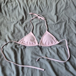 Ljusrosa trekantsbikini med knyt - Söt ljusrosa trekantsbikini med tunna band som knyts i nacken och runt ryggen. Klassisk modell med släta kupor och enkel design, perfekt för stranden eller poolen. Materialet är mjukt och stretchigt för en bekväm passform.
