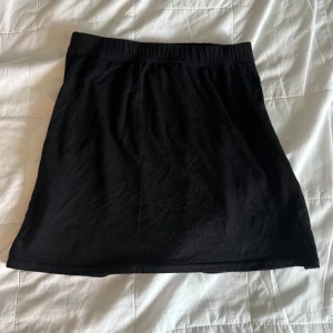 Svart kortkjol från Boohoo - Enkel svart kortkjol från Boohoo med elastisk midja. Kjolen är i mjukt material och har en klassisk rak passform som är lätt att matcha med olika toppar och sneakers.