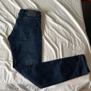 Replay Anbass mörkblå jeans herr - Snygga mörkblå Replay Anbass jeans med power stretch. Klassisk femficksmodell, normal passform och raka ben. Jeansen har diskreta Replay-detaljer och är tillverkade i mjukt denimtyg som sitter skönt hela dagen. Köpte i butik och kunde inte lämna tillbaka därför säljer jag dom medans dom max är använda 2 gånger. W 30 L 32. Vid snabb affär kan pris sänkas