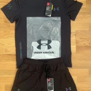 Svart t-shirt från Under Armour - Svart t-shirt från Under Armour med klassisk logga på bröstet och tryckt text längs sidan. T-shirten är kortärmad och har en sportig, stilren look som passar perfekt till träning. Materialet känns lätt och andas bra.