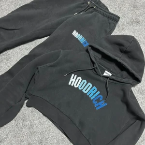 hoodie&byxor från Hoodrich - Svart croppad hoodie från Hoodrich med broderad logga i vitt och blått framtill. Byxorna har en liten skada på sidan men det syns inte när man har dem på sig.