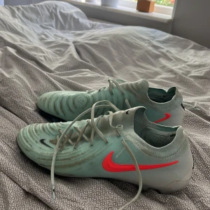 NIKE PHANTOM GX II ELITE FG MAD ENERGY - GRÖN/ATOMIC RED/RÖD - Använda cirka cirka 5 gånger, smutset pga svarta gummi i fotbollsplanen. Storlek 45, passar även lite mindre samt större. Påse tillkommer.
