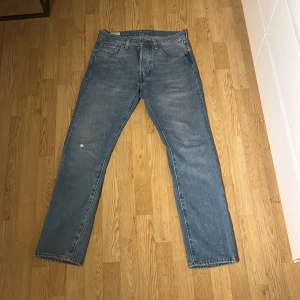 Levi's 501 ljusblå jeans W30 L32 - Klassiska Levi's 501 jeans i ljusblå denim. Rak passform med fem fickor och knappgylf. Snyggt slitna detaljer och ikonisk läderpatch bak i midjan. Perfekta för en avslappnad och tidlös stil. Är i nyskick förutom en liten slitning på framsidan och en liten slitning på baksidan.