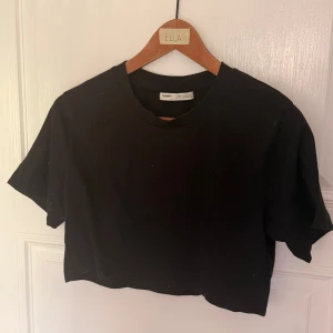 Svart croppad t-shirt från Pull&Bear - Enkel svart croppad t-shirt från Pull&Bear med rund halsringning och korta ärmar. Perfekt till jeans eller kjol för en chill och stilren look.