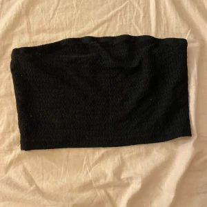 Svart bandeau tubtopp - En enkel svart bandeau tubtopp med smockad textur . Ärmlös och axelbandslös design som sitter tight mot kroppen.