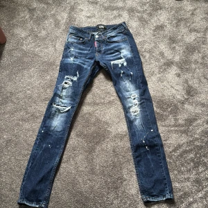 Blå slitna jeans från ICON XWAY  - Säljer ett par blå jeans från ICON XWAY med coola slitningar och distressed detaljer på benen. Jeansen har klassisk femficksdesign, raka ben och snygga kontrastsömmar. Märkespatch bak i svart och röd etikett framtill. Perfekta för en avslappnad streetstil. Liknar mycket dsquared2.