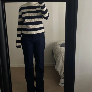 Randig ribbstickad tröja i svart och vitt - Säljer en ribbstickad tröja med breda svarta och vita ränder. Tröjan har lång ärm, hög hals och är i en skön, stretchig kvalitet. Perfekt för dig som gillar klassisk stil med en modern twist.