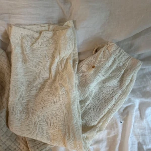 Krämvita spetsbyxor från Zara - Säljer ett par krämvita byxor från Zara med snyggt spetsmönster och resår i midjan. Byxorna har en luftig känsla och är fodrade på insidan för extra komfort. Perfekta för en chill och trendig sommarlook.
