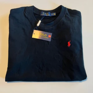 Ralph lauren t shirt - Svart t-shirt från Polo Ralph Lauren i bomull med klassisk passform. Ikoniska röda broderade loggan på bröstet och rund halsringning. Enkel och stilren design som funkar till allt. Märkeslapp kvar på tröjan.