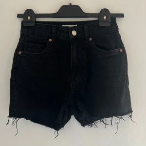 Svarta jeansshorts från H&M - Svarta jeansshorts från H&M med råa, fransiga benslut och klassisk femficksdesign. Snyggt slitna detaljer och knappstängning framtill. Perfekta för en chill sommarlook.