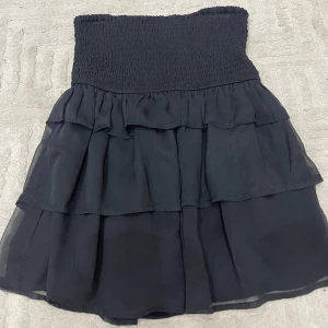 Svart volangkjol från BikBok funkar även som topp  - Supersöt svart kortkjol från BikBok i storlek XS. Kjolen har smockad midja och flera lager med volanger som ger en flowy och trendig look. Perfekt att styla med en crop top eller stickad tröja för en cool vibe. Funkar lika bra som en topp skit snygg 