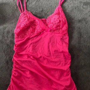 Rosa spetslinne med smala axelband - Supersöt  rosa spetslinne med smala axelband och spets upptill. Blommiga spetsdetaljer och liten rosett framtill ger en romantisk vibe. Mjuk och stretchig, perfekt för varma dagar eller när du vill känna dig extra fin.