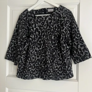 Leopardmönstrad blus från Masai - Säljer en svart och grå leopardmönstrad blus från marella. Blusen har trekvartsärmar och en snygg dragkedja bak. Den är lite loose i modellen och har rund halsringning. Perfekt för dig som gillar djurmönster och vill sticka ut.