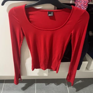 Röd långärmad topp Gina Tricot - Snygg röd långärmad topp från Gina Tricot med rundad, djup urringning. Tunn och stretchig modell som sitter tajt mot kroppen. Perfekt att styla med jeans eller kjol för en enkel men trendig look.