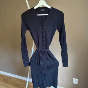 Svart ribbad klänning från SHEIN - ❤️bilder från min Vinted ❤️Svart ribbad kortklänning från SHEIN med v-ringning, långa ärmar och knappar framtill. Klänningen har ett knytband i midjan för snygg passform och är tillverkad i ett mjukt, stretchigt material. Perfekt för dig som gillar stilrena och bekväma plagg.