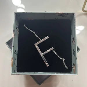 Silvrigt halsband med bokstavshänge F från Ioaku - Bokstavshalsband F från Ioaku, kedja 40+6 cm bokstan 2,8x4 cm, Nypris 499 kr, Kan gå ner i pris! kommer med original ask