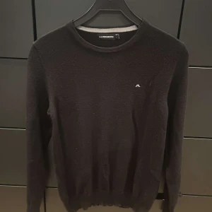Svart merinoullströja från J.Lindeberg - Stilren svart tröja från J.Lindeberg i mjuk merinoull. Klassisk rund halsringning och diskret logga på bröstet. Perfekt för dig som gillar en enkel men snygg look. Långärmad och med ribbade muddar för extra komfort. I jätte fint skick. Nypris 1300kr.