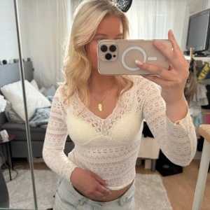Vit spetsblus med v-ringning - Säljer en superfin vit blus i spets med v-ringning och långa ärmar. Blusen är figurnära och har ett romantiskt mönster i spetsen som ger en snygg och feminin look. Perfekt att styla med jeans eller kjol för en trendig outfit.
