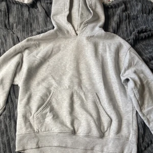 Grå hoodie från Gina Tricot - Säljer en ljusgrå hoodie från Gina Tricot, basically basics-kollektionen. Tröjan har huva, magficka och ribbade muddar vid ärmslut och nederkant. Perfekt för chill dagar eller när du vill ha en enkel och clean look.