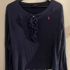 Mörkblå långärmad tröja Ralph Lauren - Supersnygg mörkblå långärmad tröja från Ralph Lauren med volangdetalj och små knappar framtill. Storlek är 16 år, skulle säga som en storlek S/M. Vet inte ifall den är äkta eller inte!!!