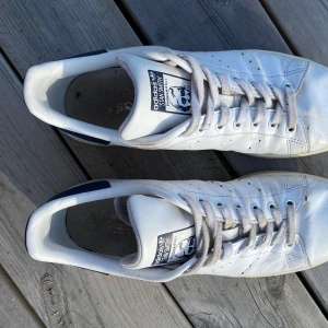 Adidas Stan Smith vita sneakers strl 42 - Klassiska Adidas Stan Smith sneakers i vitt skinn med mörkblå detaljer. Ligger ute på fler sidor först till kvarn 