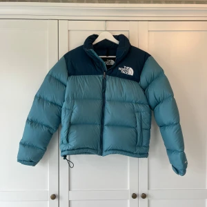Pufferjacka The North Face - Blå pufferjacka från märket the north face, som passar perfekt nu i vinter. Jackan har två fickor framtill och en innerficka. Den går även att dra in i midjan. Alla dragkedjor fungerar perfekt, så inga defekter där. Däremot har den någon enstaka liten fläck. En vid ena mudden på armen (se näst sista bilden) och en till fläck på baksidan av jackan som inte syns så tydligt (se sista bilden). De är de enda defekterna. Jackan har enbart använts en vinter. 