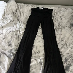 Svarta yoga pants från Gina Tricot - Svarta yoga pants från Gina Tricot med låg midja och stretchigt material. Byxorna har en bred linning och vida ben, perfekta för en chill och trendig look. Passar dig som gillar bekväma och snygga byxor.