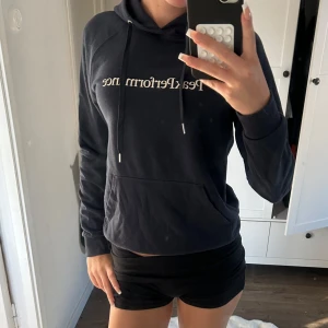 Mörkblå hoodie från Peak Performance - Mörkblå hoodie från Peak Performance med vit logga framtill. Klassisk modell med huva, snörning och känguruficka. Mjuk och skön i bomullsmix, perfekt för chill eller träning. Långärmad och normal passform.