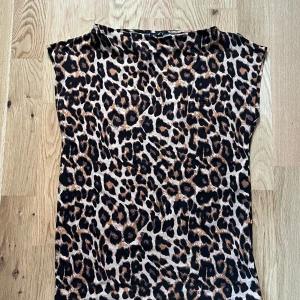 Leopardmönstrad ärmlös topp - Snygg ärmlös topp med leopardmönster i svart och bruna toner. Modellen har en rak passform och rund halsringning. Har inte använt den
