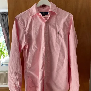 Rosa Ralph Lauren skjorta  - En sjukt snygg Ralph Lauren skjorta i gott skick. Dessvärre är det en liten fläck på vänster arm, men därav det billiga priset.