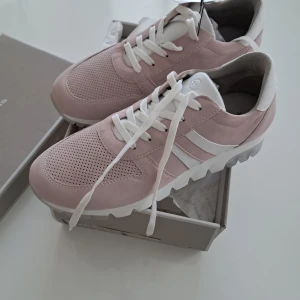Ljusrosa sneakers från Tamaris - Snygga ljusrosa sneakers från Tamaris med vit sula och vita detaljer. Ovandelen är i mocka och skinn, med perforerat mönster framtill och vita snören. Skorna har en chunky, räfflad sula som ger en cool look och extra komfort.