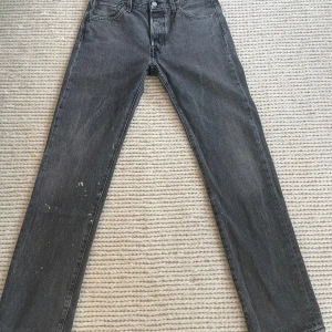 Levi's 501 svarta raka jeans W30 L32 - Säljer ett par klassiska Levi's 501 jeans i svart tvätt. Jeansen har rak passform, knappgylf och fem fickor. De är tillverkade i robust bomullsdenim och har den ikoniska läderpatchen bak. Bra passform, dock små ljusa fläckar på vänster ben